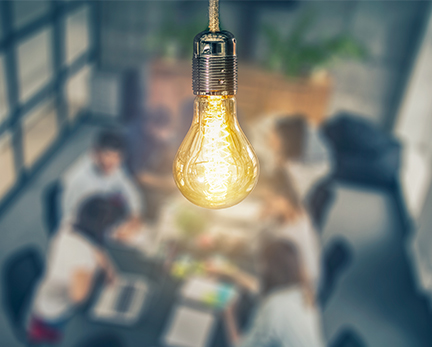 SRM Our Approach image - Lightbulb with people at desk.
