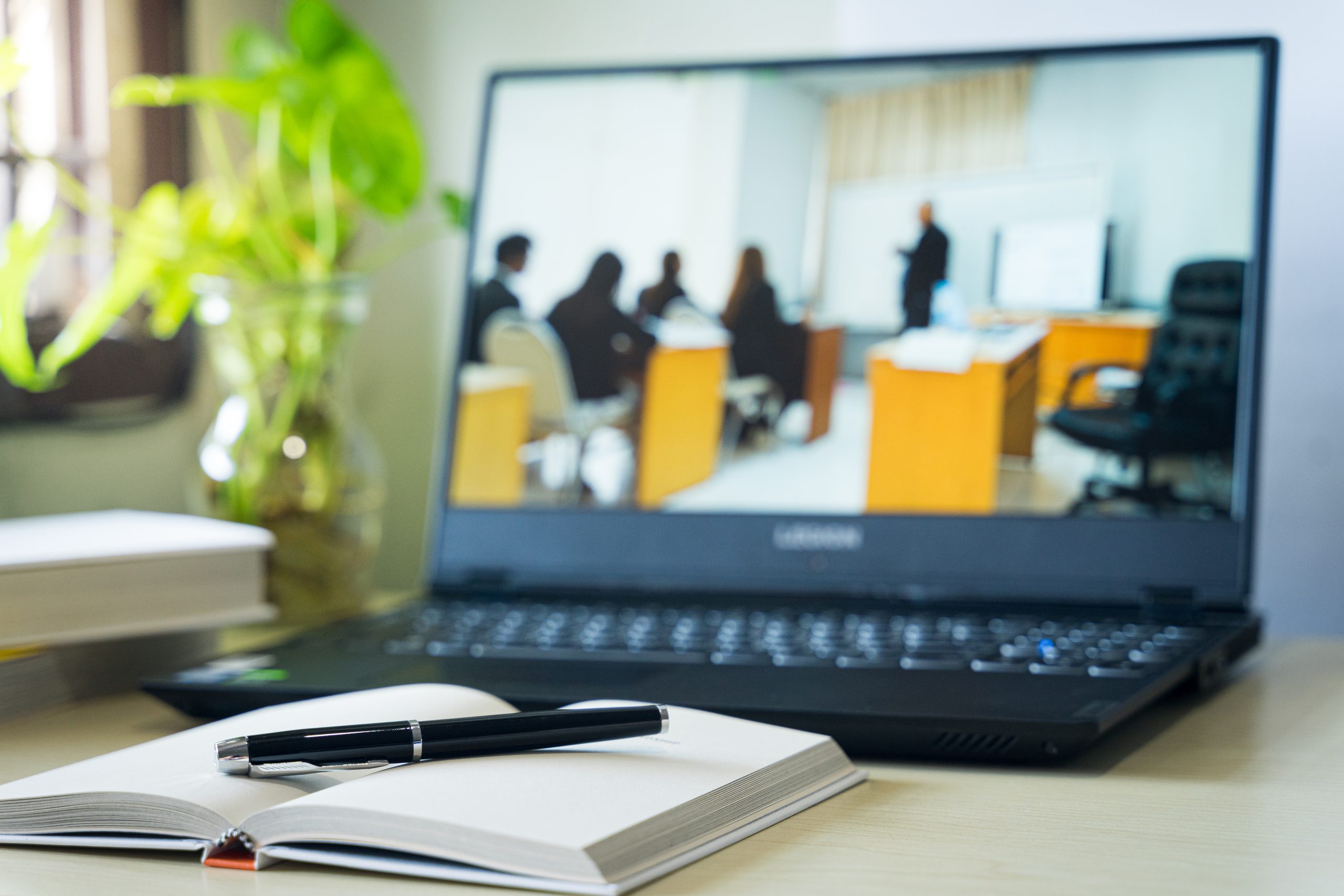 Desk with notebook and laptop displaying virtual classroom.