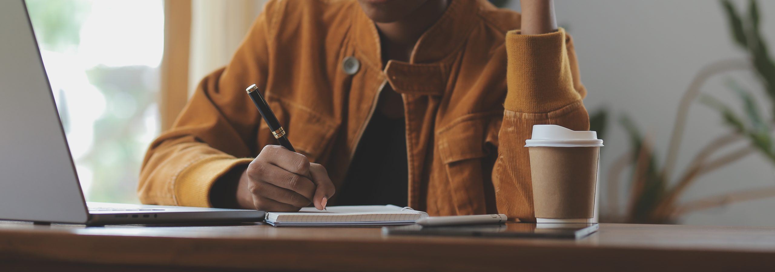 Adult learner studying at desk with laptop and notebook.
